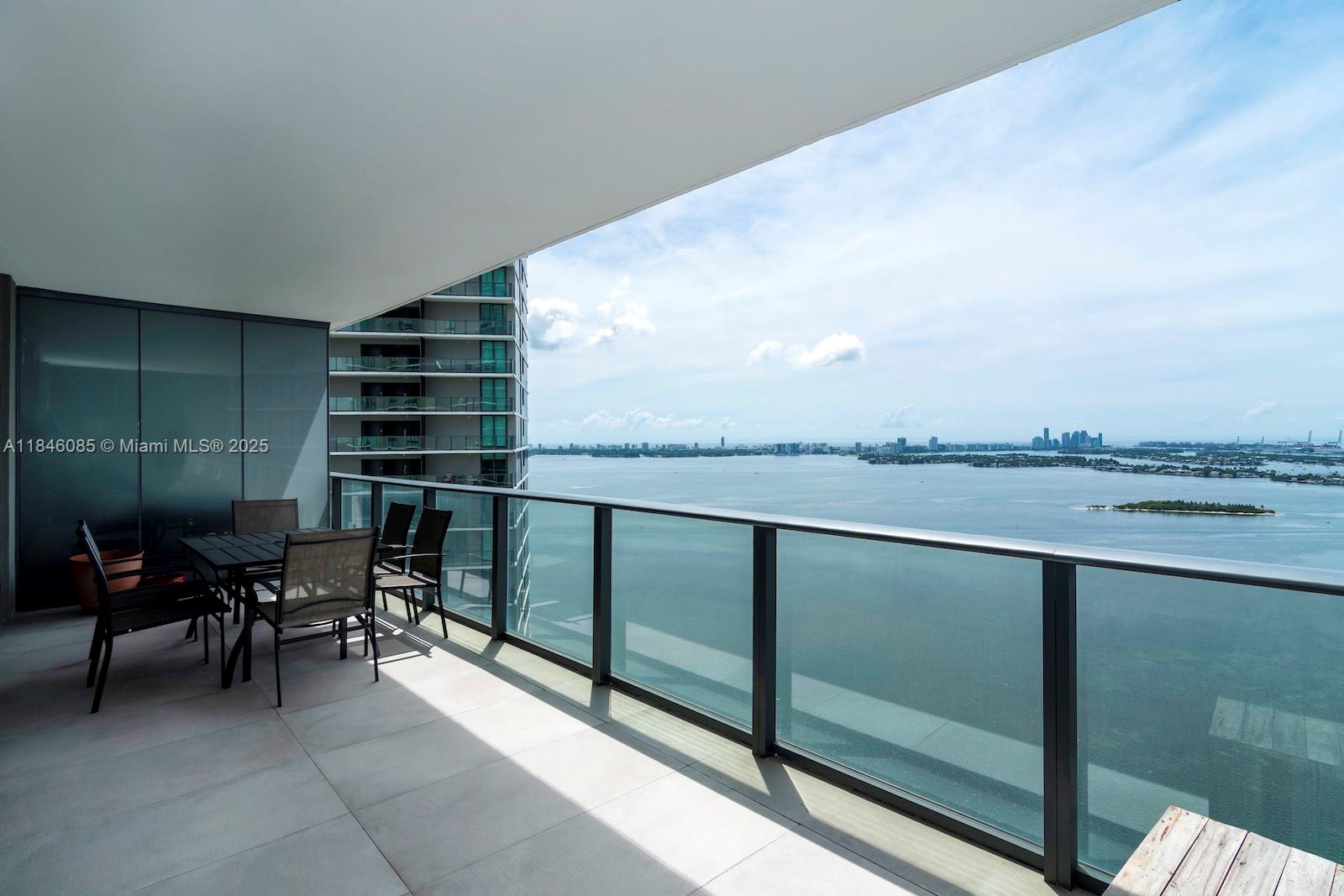 A high-rise balcony features a dining set overlooking a bay and city skyline — 650 NE 32nd St # 4206, Miami FL 33137, MIAMI, FL