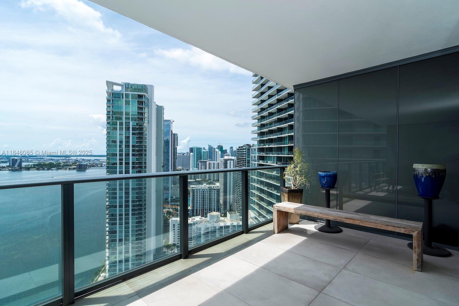A high-rise balcony features a wooden bench, two blue planters, and panoramic city and water views — 650 NE 32nd St # 4206, Miami FL 33137, MIAMI, FL