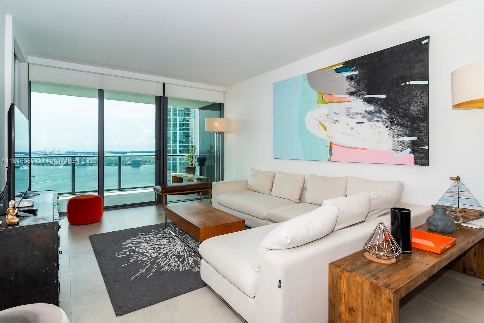 A modern living room features a white sectional sofa, abstract wall art, and balcony views — 650 NE 32nd St # 4206, Miami FL 33137, MIAMI, FL