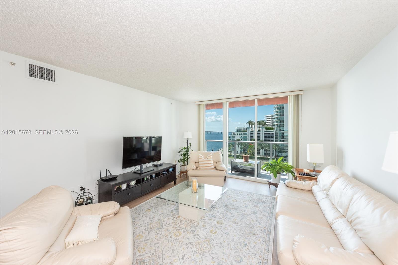 A living room features cream leather sofas, a glass coffee table, and a balcony view — 1155 Brickell Bay Dr # 609, Miami FL 33131, MIAMI, FL