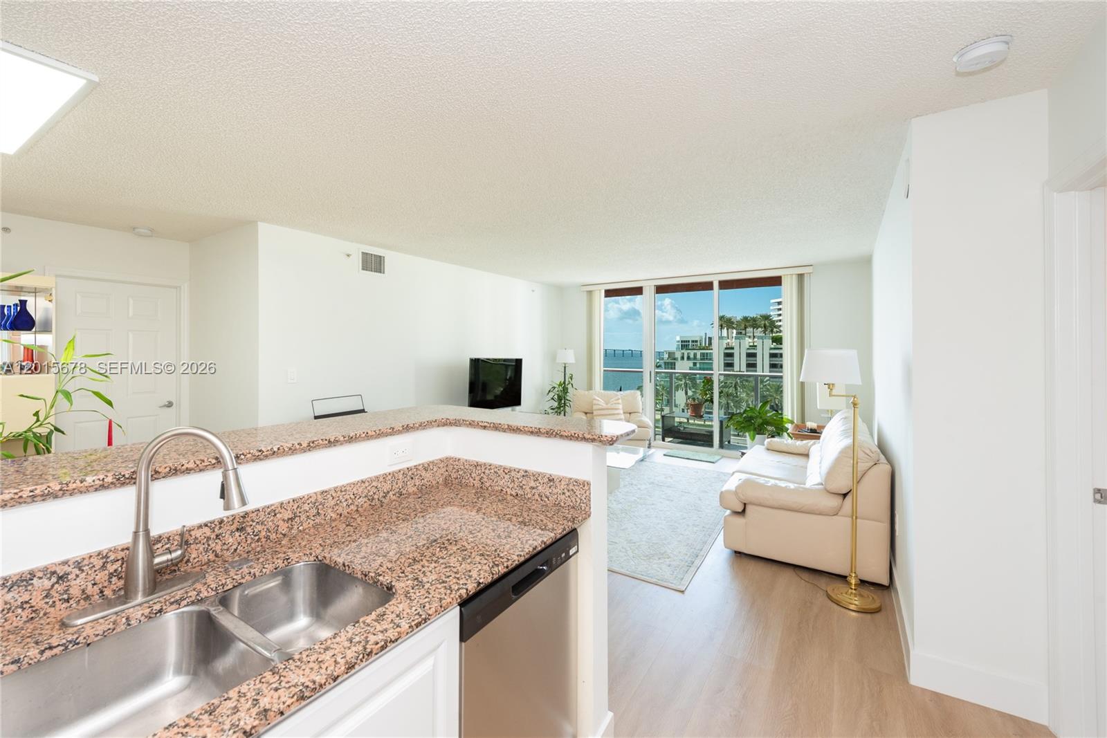 A kitchen with granite countertops overlooks a living room with a balcony and water view — 1155 Brickell Bay Dr # 609, Miami FL 33131, MIAMI, FL