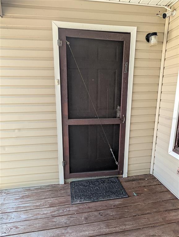 A brown screen door with a diagonal tension cable leads to an entrance with siding — 2004 2ND AVENUE E UNIT 1, BRADENTON, FL