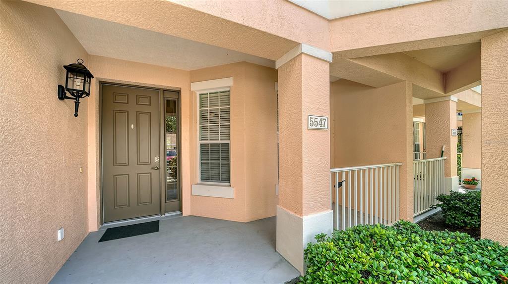 The exterior entrance features a tan door, a window, and a covered porch with railings — 5547 KEY WEST PLACE UNIT C-01, BRADENTON, FL