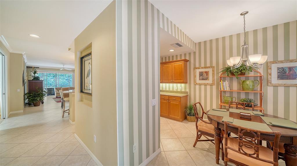 A dining area with striped wallpaper, a wooden table, and an adjacent kitchen with wood cabinets — 5547 KEY WEST PLACE UNIT C-01, BRADENTON, FL