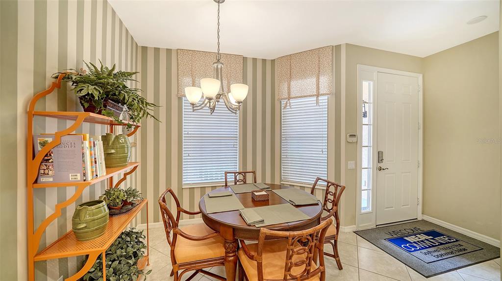 A dining area features striped wallpaper, a round wooden table, and an orange metal shelving unit — 5547 KEY WEST PLACE UNIT C-01, BRADENTON, FL