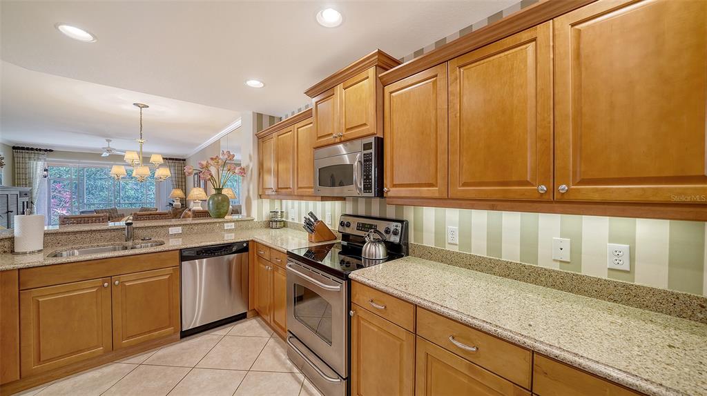 A kitchen with wood cabinets, granite countertops, stainless steel appliances, and striped wallpaper — 5547 KEY WEST PLACE UNIT C-01, BRADENTON, FL