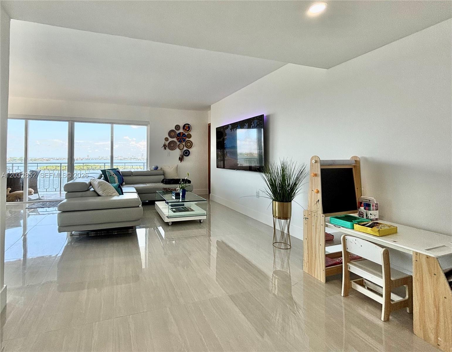 A modern living room features light tile floors, a sectional sofa, and a balcony view — 11111 NE Biscayne Blvd # 16A, Miami FL 33181, MIAMI, FL