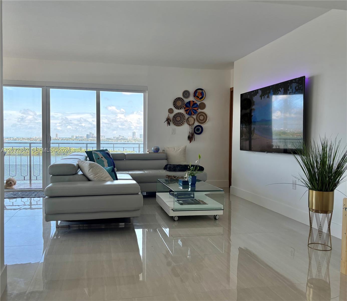 A living room features a gray sectional sofa, glass coffee table, and a wall-mounted television — 11111 NE Biscayne Blvd # 16A, Miami FL 33181, MIAMI, FL