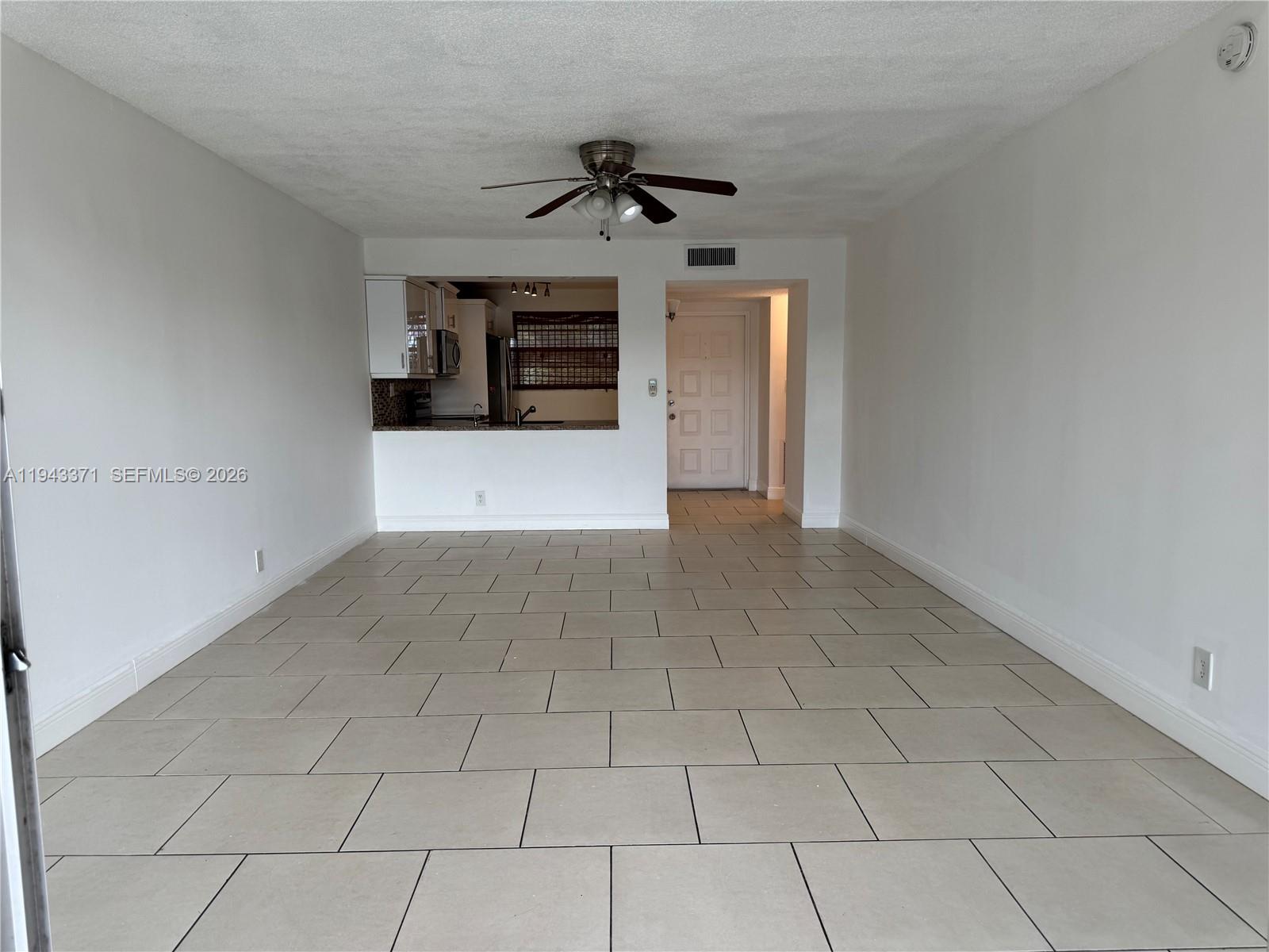 A living area with light-colored tile flooring, white walls, and an open kitchen pass-through — 1831 Sabal Palm Dr # 403, Davie FL 33324, DAVIE, FL