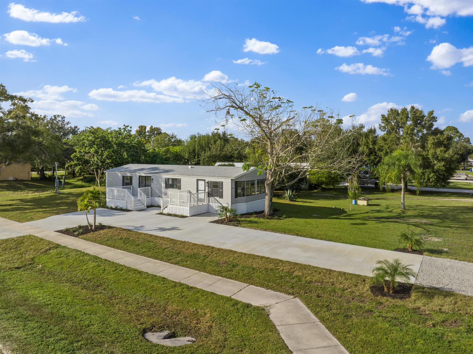 A light gray manufactured home features white decks and a large concrete driveway — 218 S Maple St, Fellsmere FL 32948, FELLSMERE, FL