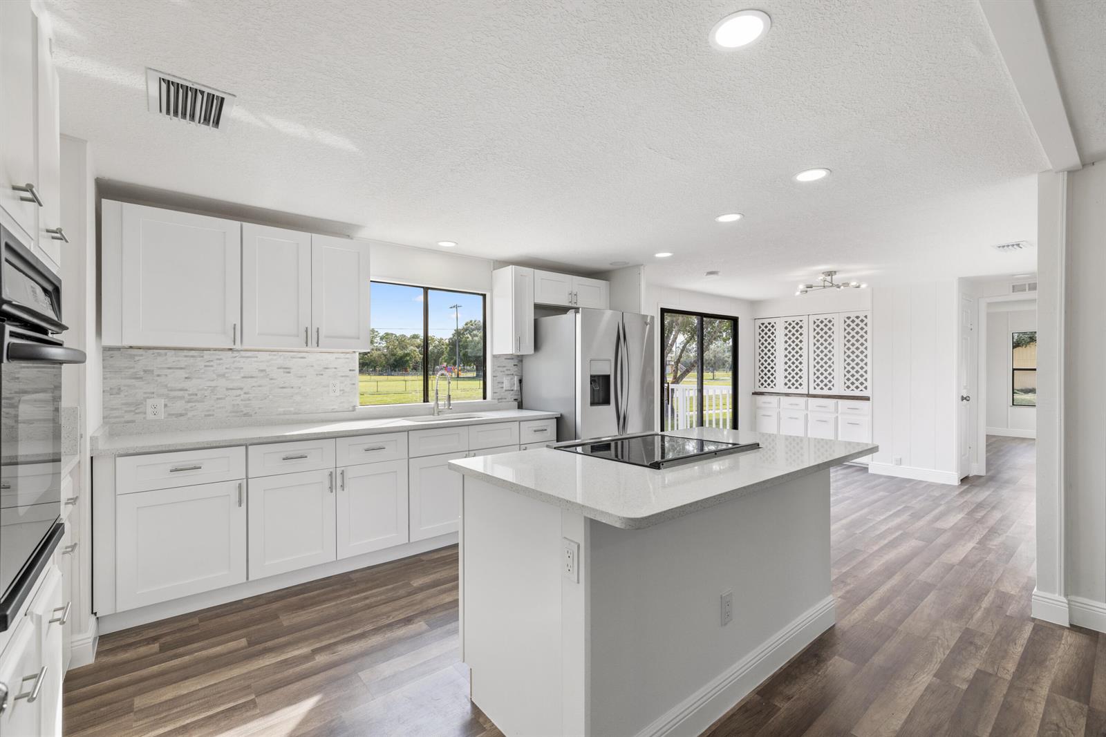 A bright kitchen features white cabinetry, a central island with a cooktop, and wood-look flooring — 218 S Maple St, Fellsmere FL 32948, FELLSMERE, FL