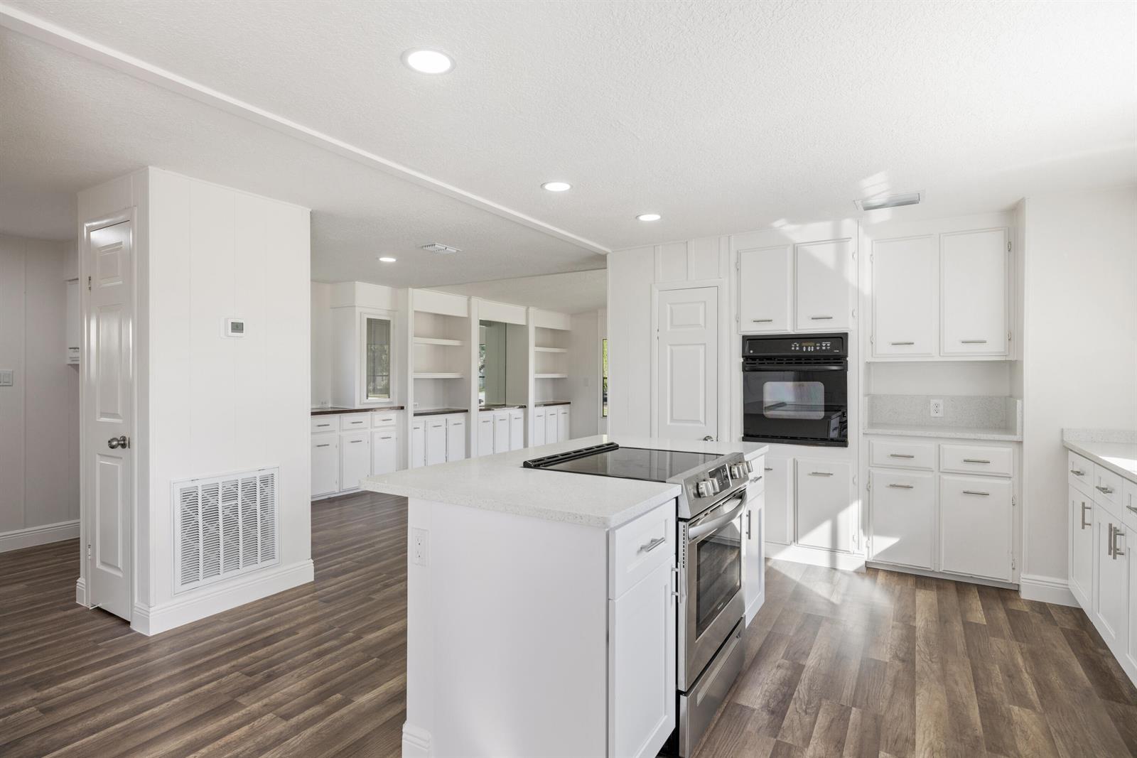A bright kitchen features white cabinets, a central island with a stove, and wood-look flooring — 218 S Maple St, Fellsmere FL 32948, FELLSMERE, FL