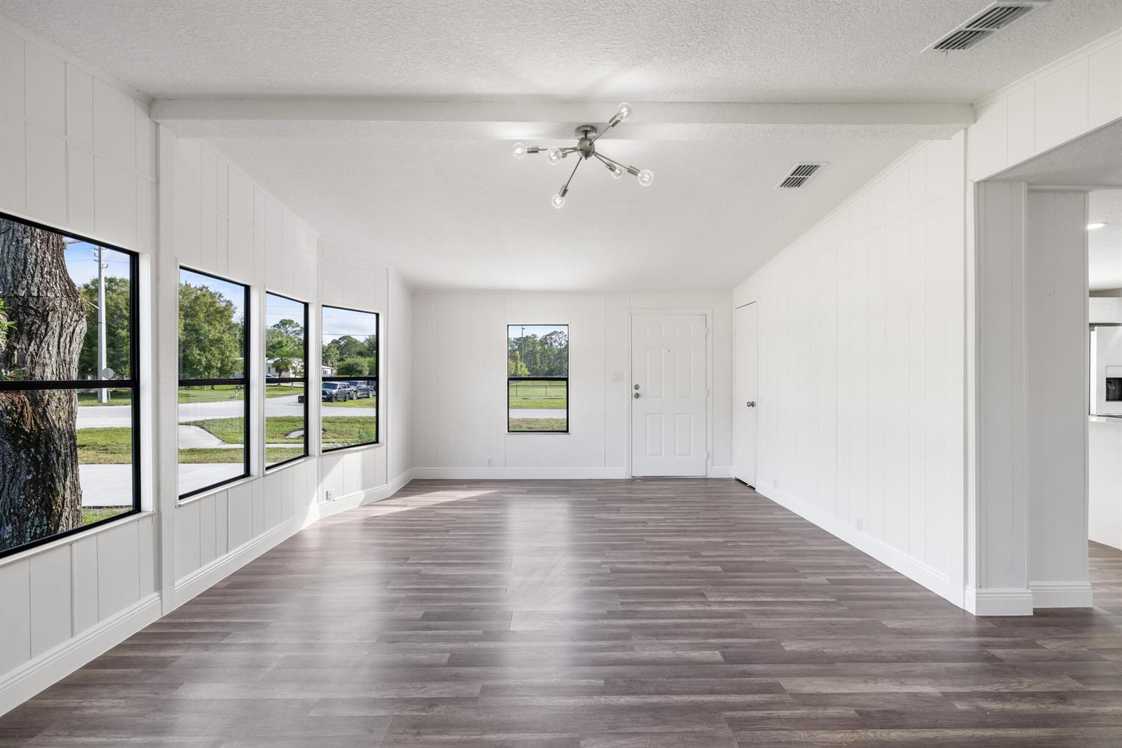 An empty room features white paneled walls, wood-look flooring, and a modern sputnik light fixture — 218 S Maple St, Fellsmere FL 32948, FELLSMERE, FL