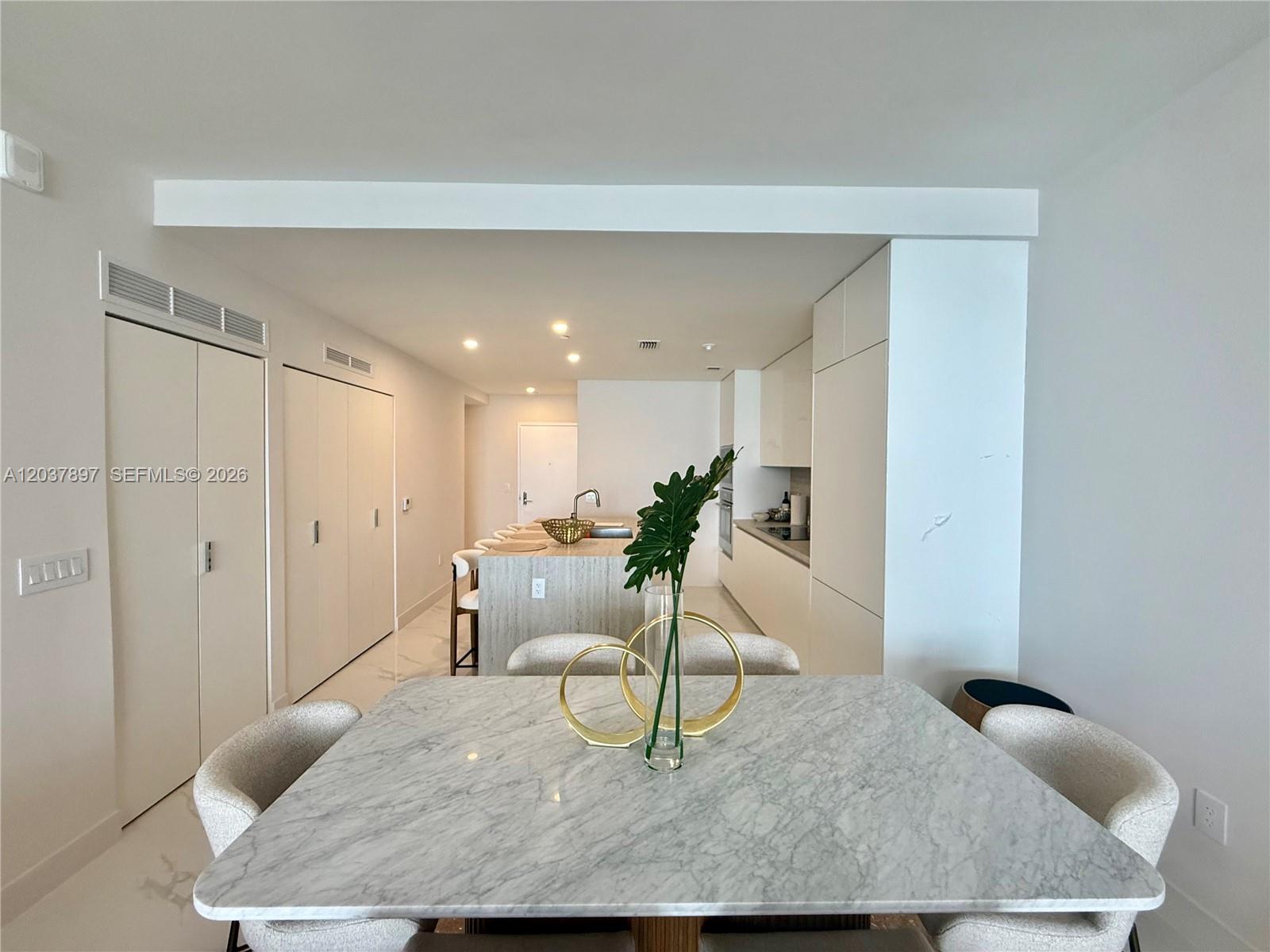 A dining area with a marble table leads into an open-concept kitchen with stone counters — 700 NE 24th St # 1002, Miami FL 33137, MIAMI, FL