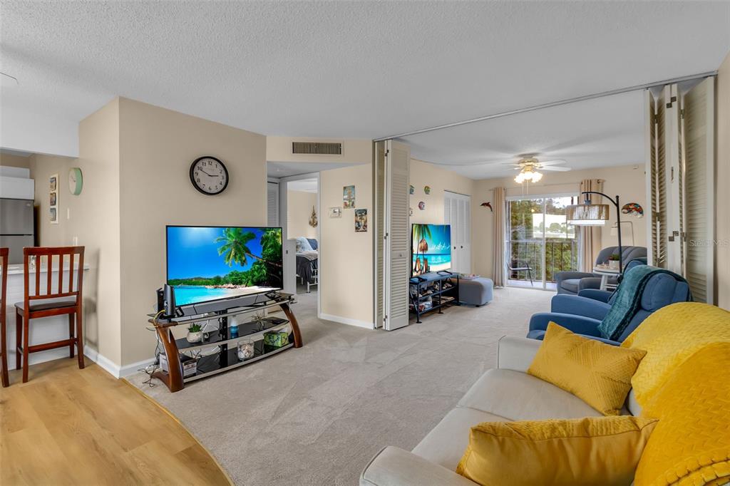 A living room features a television, a sofa with yellow pillows, and a balcony view — 4210 IRONWOOD CIRCLE UNIT 403J, BRADENTON, FL
