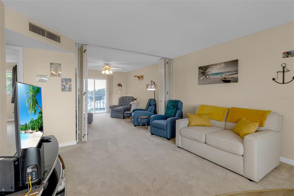 A living room with beige carpet, a white sofa, blue armchairs, and a sliding glass door — 4210 IRONWOOD CIRCLE UNIT 403J, BRADENTON, FL