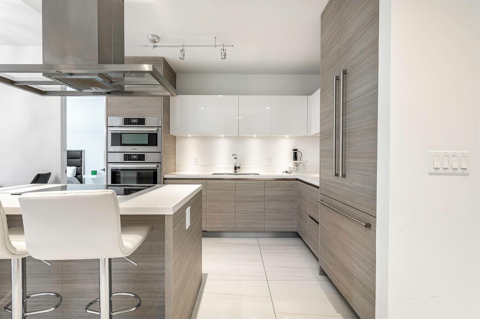 A modern kitchen features wood-grain cabinetry, white upper cabinets, stainless steel appliances, and a breakfast island — 155 E Boca Raton Road # 415, Boca Raton FL 33432, BOCA RATON, FL