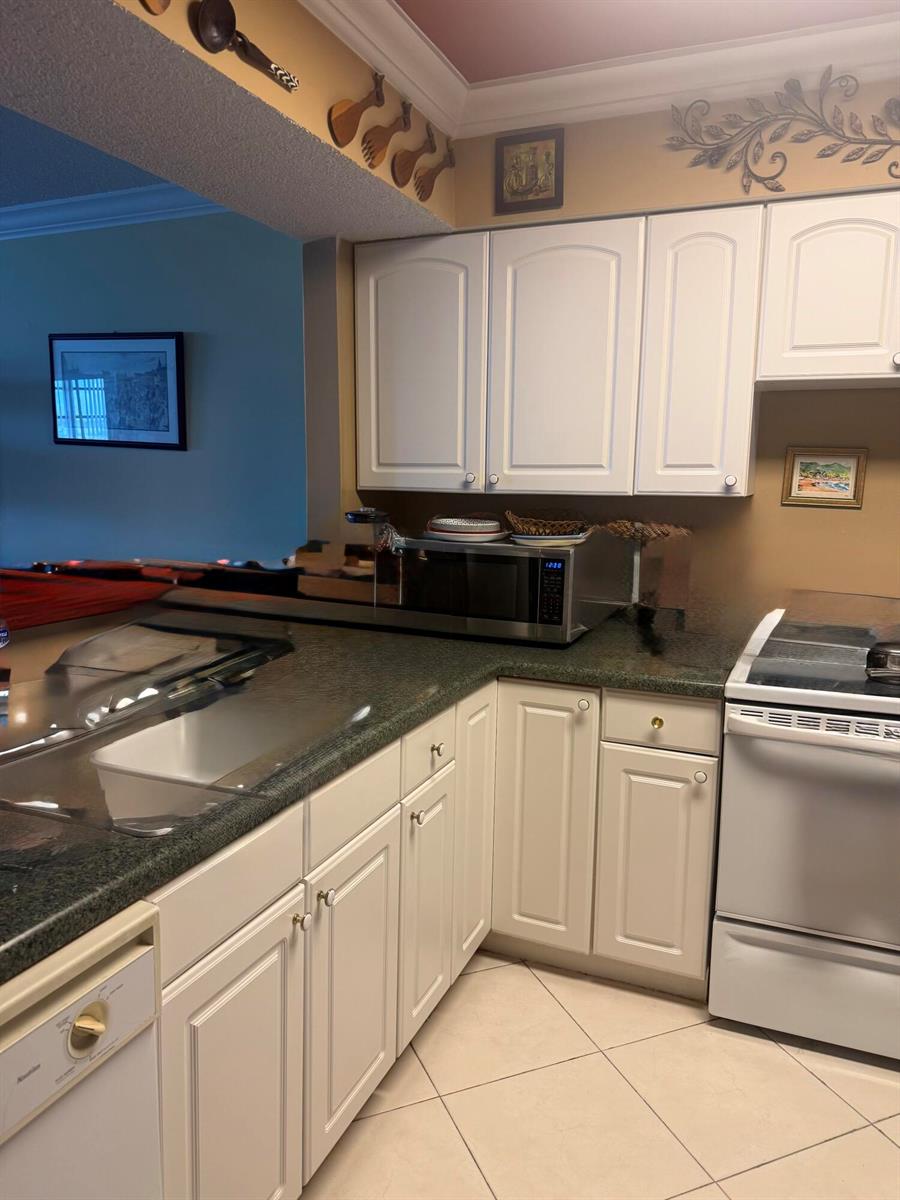A kitchen features white cabinets, dark countertops, a microwave, and light-colored tile flooring — 2900 N Course Drive # 1005, Pompano Beach FL 33069, POMPANO BEACH, FL