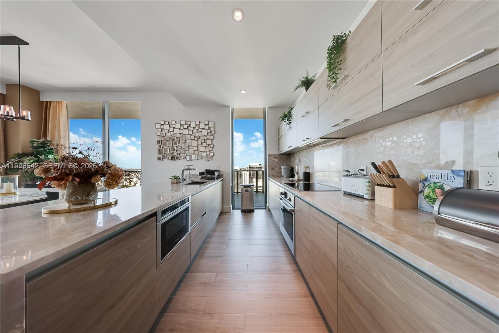 A modern galley kitchen features light wood cabinetry, marble countertops, and a balcony view — 1300 S Miami Ave, Miami FL 33130, MIAMI, FL