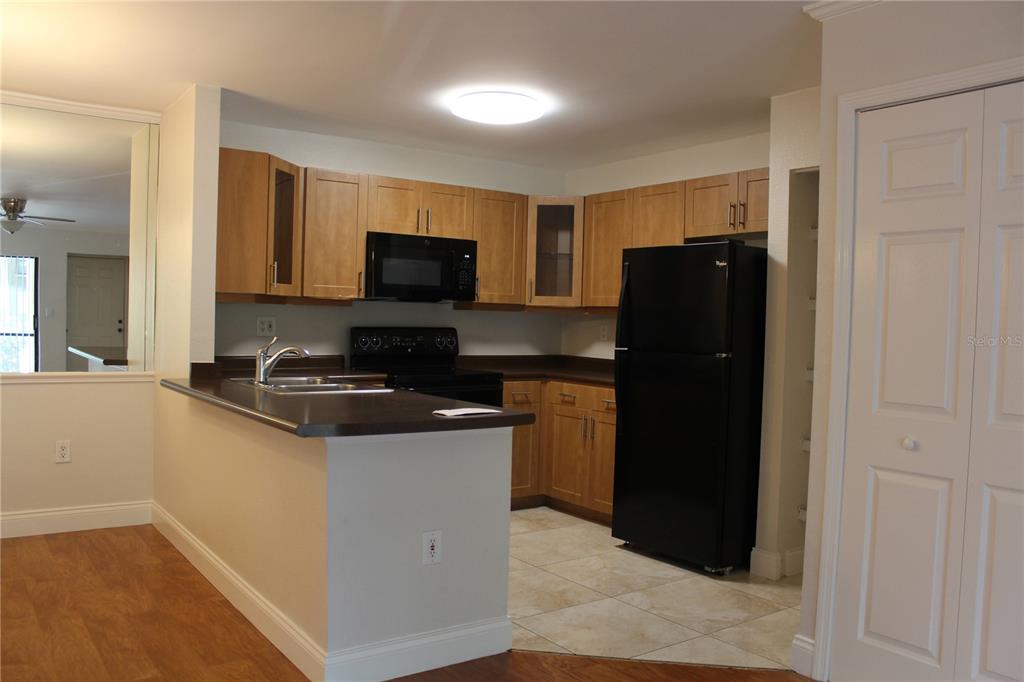 A kitchen features light wood cabinets, dark countertops, black appliances, and tile flooring — 5602 BAYWATER DRIVE, TAMPA, FL