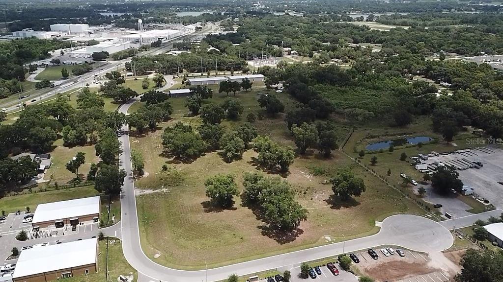 An aerial view shows a vacant grassy lot surrounded by trees, roads, and commercial buildings — 1080 DUCK BOX ROAD, UMATILLA, FL