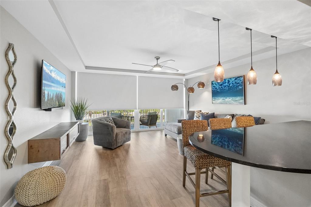 A modern living room and kitchen area with light wood floors and a balcony view — 223 ISLAND WAY UNIT 4C, CLEARWATER BEACH, FL