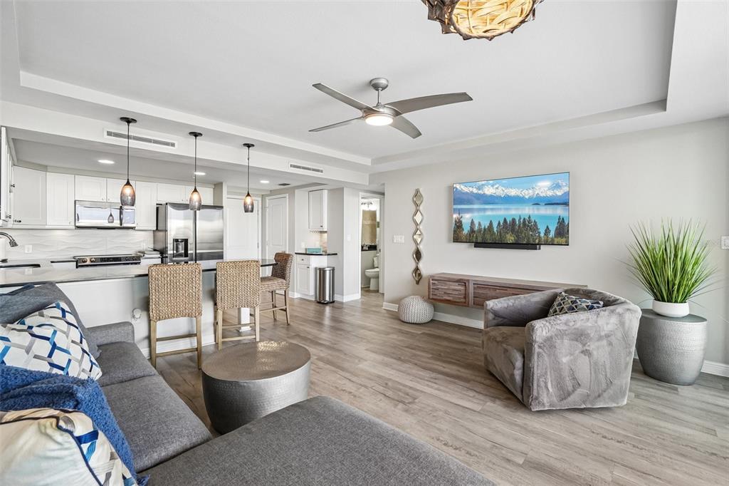 A living room with gray furniture, a wall-mounted television, and an open kitchen with stools — 223 ISLAND WAY UNIT 4C, CLEARWATER BEACH, FL