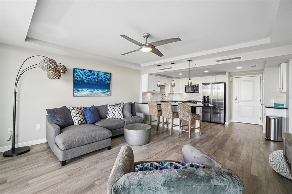 A modern open-concept living room and kitchen with gray furniture, wood floors, and pendant lighting — 223 ISLAND WAY UNIT 4C, CLEARWATER BEACH, FL