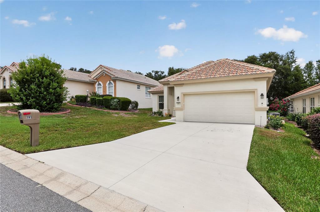 A single-story house with a beige stucco exterior, a tiled roof, and a concrete driveway — 191 W DOERR PATH, HERNANDO, FL