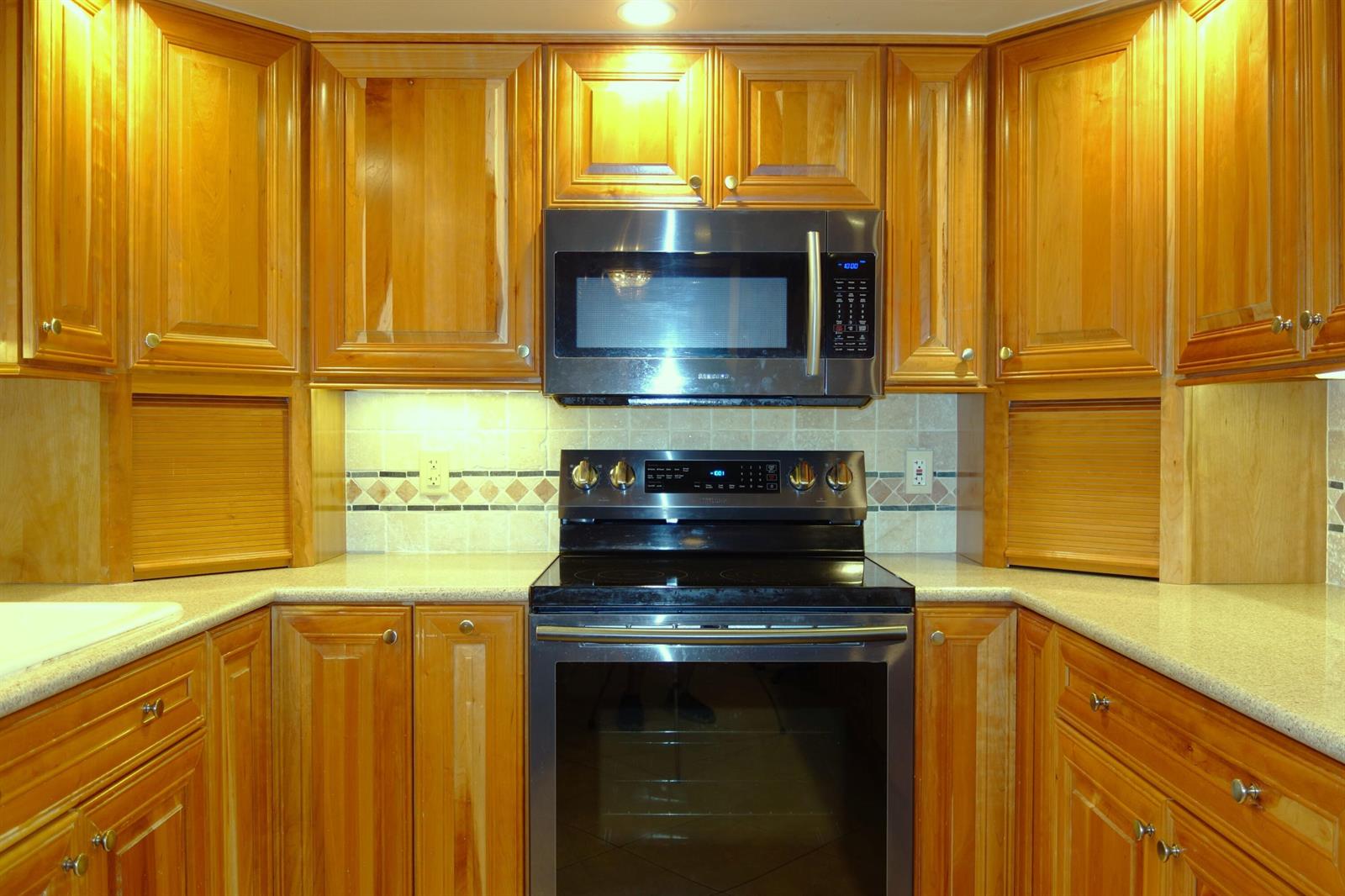 A kitchen features wood cabinets, stainless steel appliances, and a tiled backsplash with decorative accents — 3507 Oaks Way # 307, Pompano Beach FL 33069, POMPANO BEACH, FL