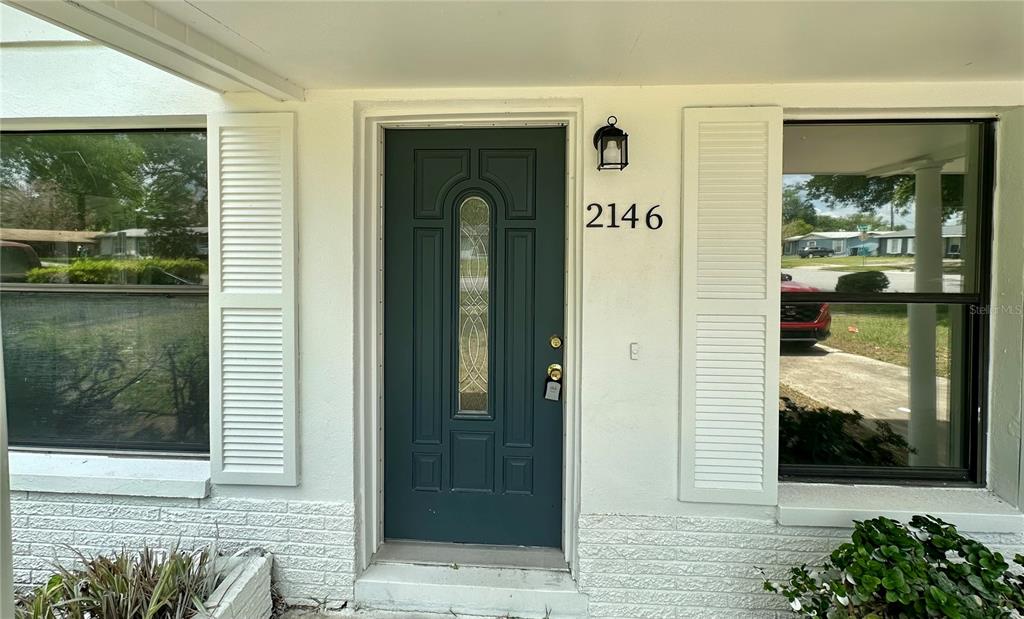 A teal front door with a glass insert is centered between two windows with shutters — 2146 AARON AVENUE, ORLANDO, FL
