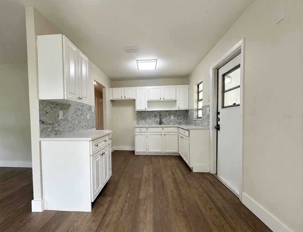 A kitchen features white cabinets, a mosaic tile backsplash, and wood-look flooring — 2146 AARON AVENUE, ORLANDO, FL