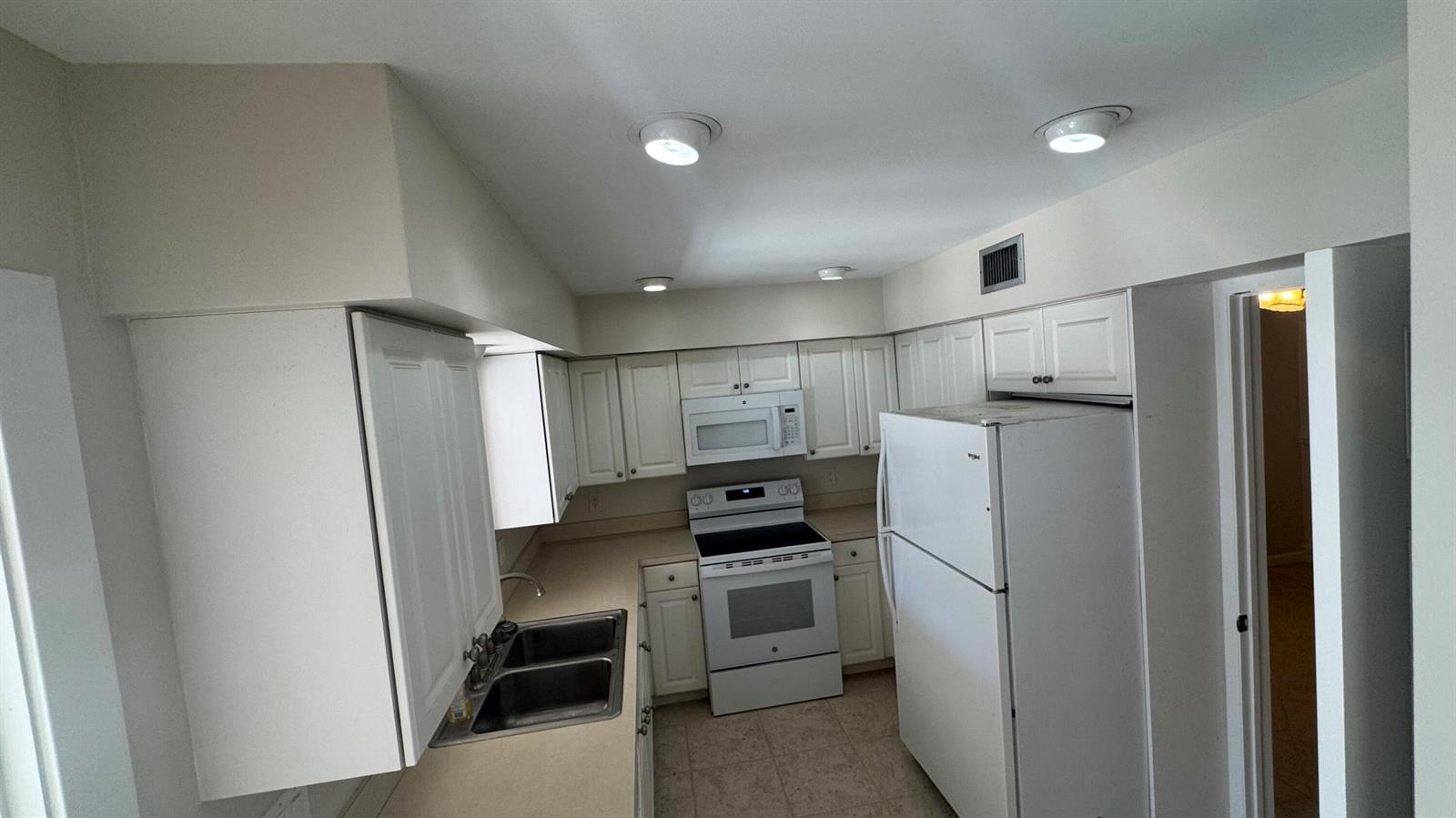 A kitchen features white cabinets, a white stove, a white refrigerator, and a double sink — 2704 Cardinal Drive, Vero Beach FL 32963, VERO BEACH, FL