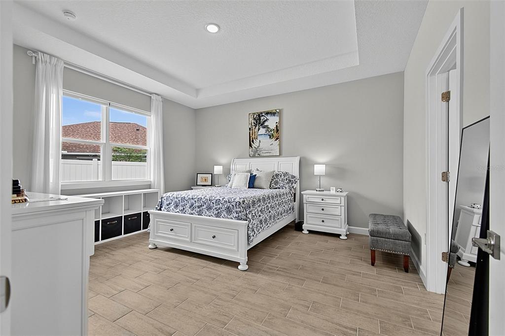 A bedroom features a white bed, light wood-look tile flooring, and a tray ceiling — 30 POPLAR DRIVE, PALM COAST, FL