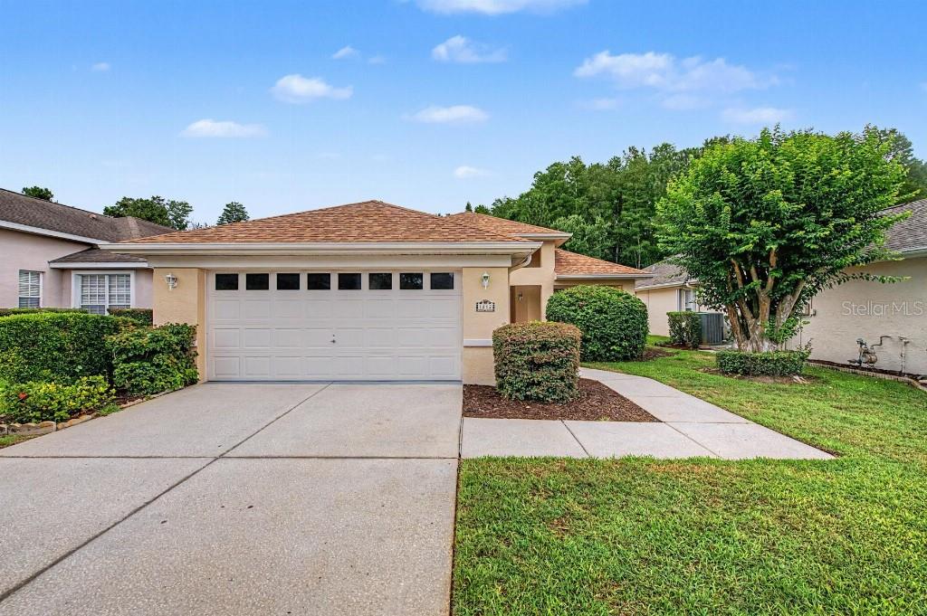 A single-story house with a tan stucco exterior, a two-car garage, and a concrete driveway — 1812 ORCHARDGROVE AVENUE, NEW PORT RICHEY, FL