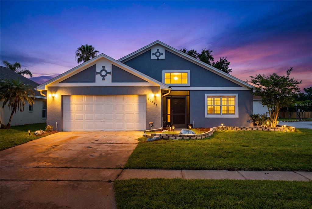 A blue single-story house with a two-car garage and a landscaped front yard at dusk — 10057 SANDBAR STREET, ORLANDO, FL