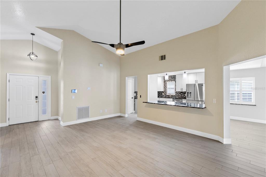 A living room with vaulted ceilings, light wood-look tile floors, and a kitchen pass-through window — 10057 SANDBAR STREET, ORLANDO, FL