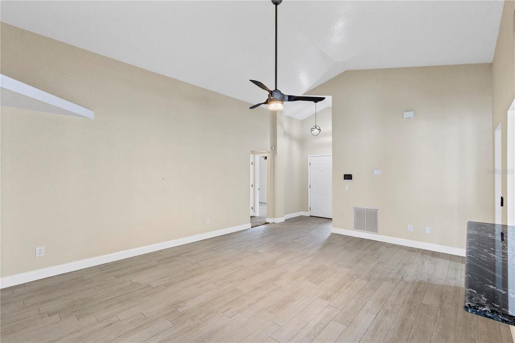 An empty living room with vaulted ceilings, a ceiling fan, and light wood-look tile flooring — 10057 SANDBAR STREET, ORLANDO, FL