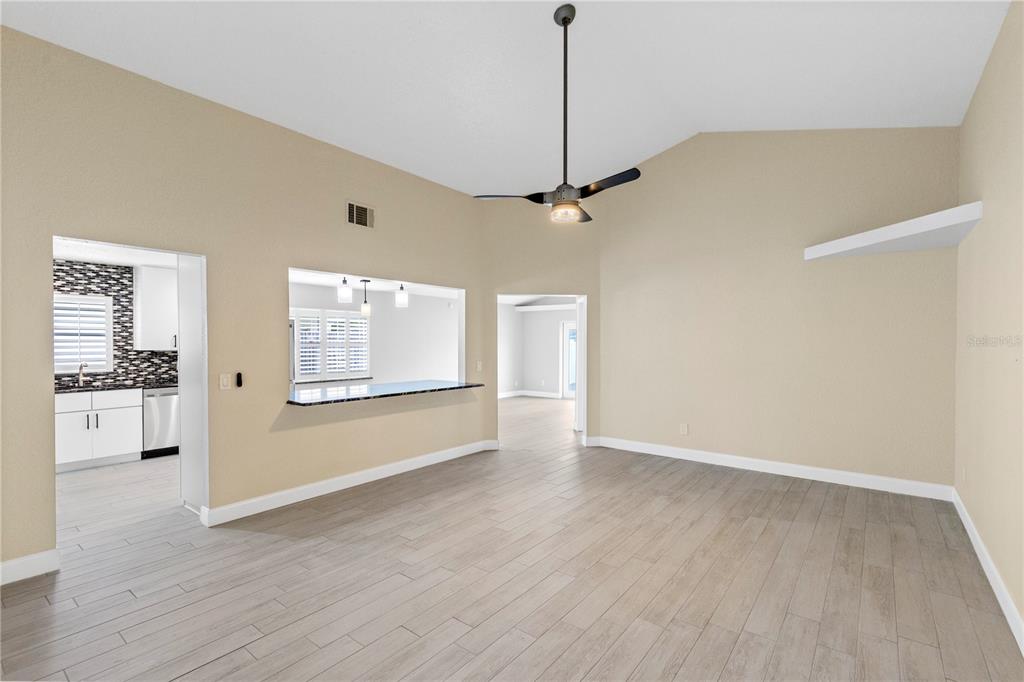 A living room with light-colored tile flooring, beige walls, a ceiling fan, and a pass-through window — 10057 SANDBAR STREET, ORLANDO, FL