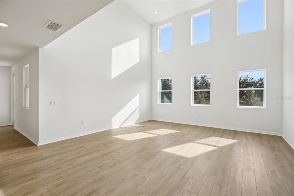 A bright, empty living room with high ceilings, large windows, and light wood-look flooring — 17625 LAKE STAR ROAD, WINTER GARDEN, FL