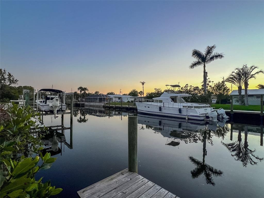 A canal view at sunset features a wooden dock, a small boat, and a large yacht — 907 22ND AVENUE W, PALMETTO, FL