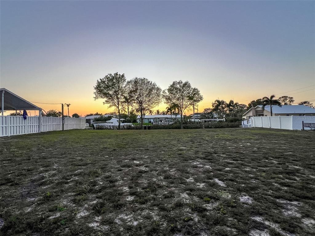 A vacant, grassy residential lot features a white fence and trees against a sunset sky — 907 22ND AVENUE W, PALMETTO, FL
