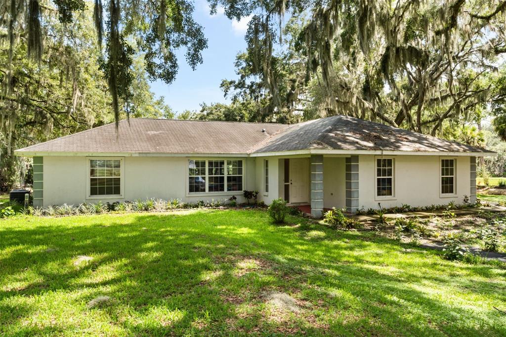 A single-story house with a white exterior, gray roof, and large windows sits on grass — 7938 JACKSONS RIVER ROAD, LEESBURG, FL