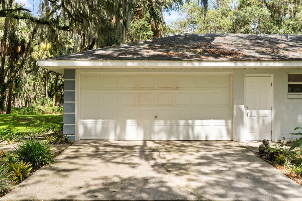 A concrete driveway leads to a white two-car garage door and an adjacent side entry door — 7938 JACKSONS RIVER ROAD, LEESBURG, FL