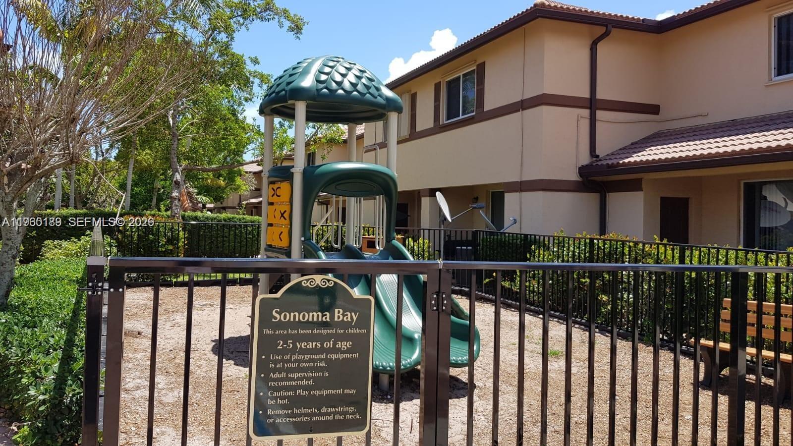 A playground with a slide and a safety sign sits behind a black metal fence — 3525 Sonoma Dr, Riviera Beach FL 33404, RIVIERA BEACH, FL