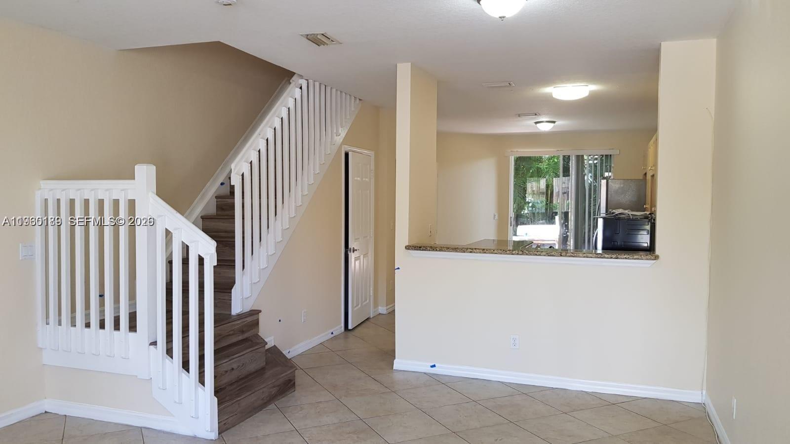 An interior view shows a staircase with white railings next to an open kitchen area — 3525 Sonoma Dr, Riviera Beach FL 33404, RIVIERA BEACH, FL