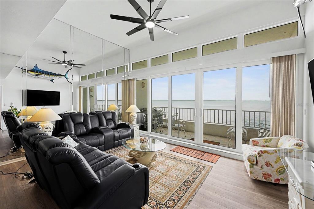 A living room features black leather recliners, a mirrored wall, and floor-to-ceiling windows overlooking water — 5279 ISLA KEY BLVD S UNIT 410, ST PETERSBURG, FL