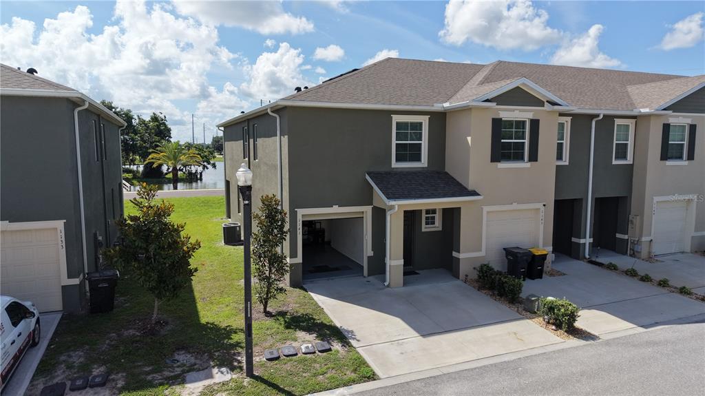 An aerial view shows a multi-unit townhouse exterior with attached garages and a nearby pond — 1141 BLUE JAY DRIVE, DAVENPORT, FL