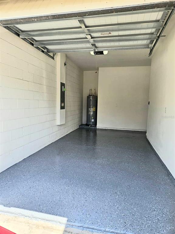 A garage with a gray epoxy floor, white cinder block walls, and a water heater — 1141 BLUE JAY DRIVE, DAVENPORT, FL