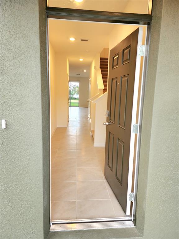 An open front door reveals a tiled entryway leading to a staircase and rear window — 1141 BLUE JAY DRIVE, DAVENPORT, FL